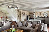 Gemütliche Eckcouch mit Kissen in grau-braunem Farbton, seitlich Treppenaufgang in offenem Wohnraum mit Küchenbereich im Hintergrund