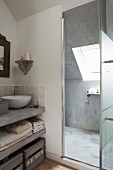 Concrete washstand counter with white countertop basin next to open glass door with view into shower area