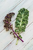 A green kale leaf and a purple kale leaf on a wooden surface