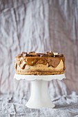 A Snickers cheesecake with caramel ganache on a cake stand