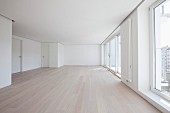 Spacious, empty room in apartment with laminate floor, white walls & floor-to-ceiling windows