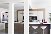 Island counter, white worksurface on brown base unit and bar stools in open-plan kitchen in loft-style apartment