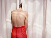 Young topless woman sticking head between curtains