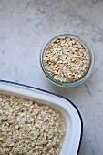 A jar of organic oats and softened oats in an enamel dish on a marble surface