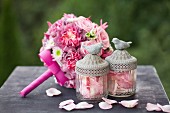 Romantic bridal bouquet with pink roses, scattered rose petals and glass jars with bird figurines on lids
