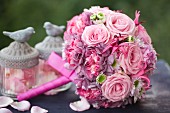 Romantischer Hochzeitsstrauß mit rosafarbenen Rosen und Glasgefäßen mit Vogelfiguren gefüllt mit Rosenblütenblättern