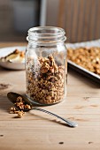 Granola in a storage jar and on a baking tray in the background