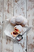 Four jam doughnuts on a piece of parchment paper on a wooden surface