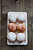 Six doughnuts, iced and dusted with icing sugar, on a paper tray (seen from above)