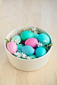 Coloured Easter eggs with flowers and straw in a bowl