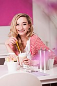 Junge Frau sitzt an Tisch eines Cafes & trinkt Latte Macchiato