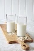 Two glasses of vegan oat milk with oats on a chopping board