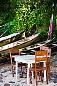 Tisch und Stühle am Strand neben alten Holzbooten