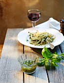 Spaghetti with basil pesto and a glass of red wine on a wooden table