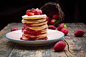 A stack of pancakes with strawberries and strawberry jam on a plate