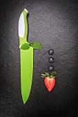 An arrangement featuring blueberries, a strawberry and green knife on a slate surface