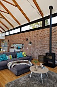 Loungebereich mit Couchtisch auf Flokatiteppich und graues Sofa in offenem Wohnraum mit sichtbarem Dachstuhl und Ziegelwand