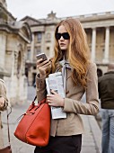 Junge Frau in sandfarbenem Blazer mit Smartphone