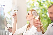 Personen bei Weinverkostung: Mann & Frau betrachten Weißwein in Weingläsern
