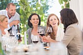 Junge Frauen bei der Weinverkostung an Tisch im Freien: Kellner zeigt Weinflasche