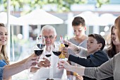 A family eating together at a terrace table: raising a toast with glasses of red wine and lemonade