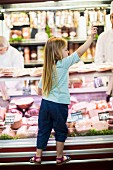 A little girl standing at a meat counter
