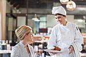 Chefköchin serviert blonder Dame Hauptgericht in Restaurant