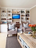 Gemütliches Wohnzimmer mit weißem Einbauregal, Fernseher und beigefarbenen Sesseln