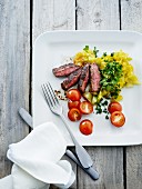 Beef steak with a herb potato salad, gherkins and tomatoes