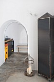 Cupboard made from riveted metal panels and candles in birdcage next to arched doorway leading into kitchen