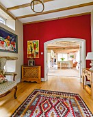 Folkloristischer Teppich mit rot getönter Wand und Durchgang, Blick in offenen Wohnraum