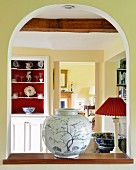 Durchreiche mit Rundbogen, auf Fensterbrett kunsthandwerkliche Vase und Blick auf Regalschrank neben offener Tür