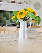 Sonnenblumenstrauß in weißem Krug auf Holztisch in Landhausküche