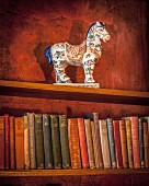 Antiquarische Büchersammlung mit kunsthandwerklicher Porzellan- Pferdefigur auf Holzregal in Bibliothek