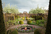 Fountain in centre of circular flowerbed and gravel path surrounded by box hedges in gardens