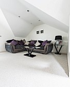 Corner sofa under sloping ceiling with recessed spotlights in elegant minimalist interior