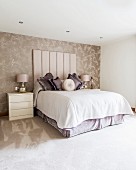 Double bed with tall upholstered headboard against patterned wallpaper in elegant bedroom