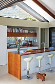 White, designer bar stools at free-standing kitchen counter with wooden top and sides in open-plan kitchen
