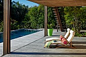 Sonnenliegen mit hellen Polstern und Rolle, auf grosszügiger Holzterrasse mit Überdachung, gegenüber Pool in tropischem Garten