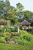 Blumenbeet mit Vintage Brunnenpumpe, im Hintergrund Pavillon in tropischem Garten