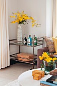 View across coffee table to vase of yellow flowers on retro serving trolley in corner of living room