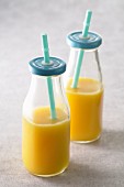 Orange juice in glass bottles with lids and straws
