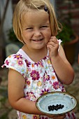 Cheerful girl wearing floral summer dress holding vintage plate of blackcurrant