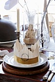 Place setting with party hat on white plate in front of Jesus figurine under glass cover