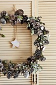 Festive wreath of pine cones with star pendant hung in vintage louvre door