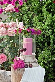 Windlicht mit rosa Kerze und Blumenkranz aus pinkfarbenen Bartnelken im Garten