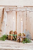 Lit candles in candle holders made from pine cone bundles tied with checked ribbons