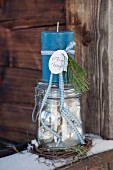 Advent arrangement of blue candle on top of vintage-style preserving jar on snowy wooden board