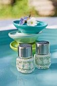 Salz- und Pfefferstreuer mit selbstgehäkelter Hülle auf türkisfarbenem Gartentisch