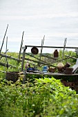 Töpferware und Gartenwerkzeug auf Vintage Holzgestell vor Gartenzaun